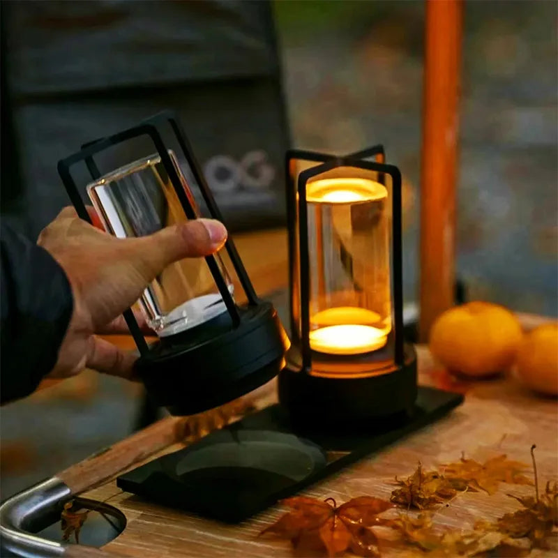 Original product photograph showing the compact black lamp held in one hand beside a second illuminated lamp