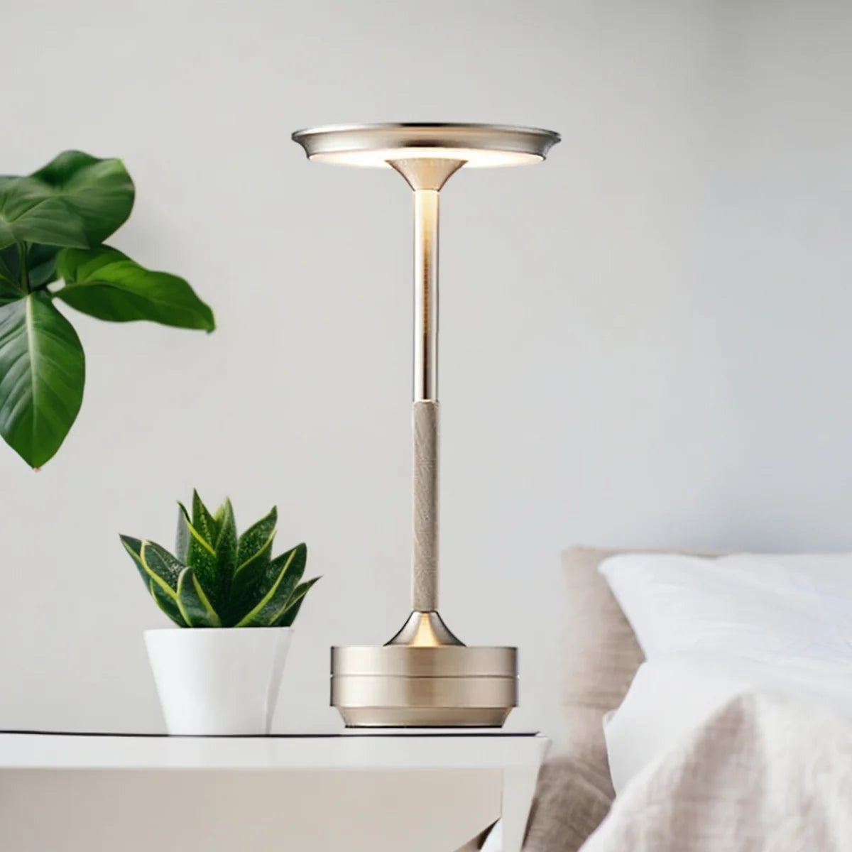 Silver Aura lamp lit on a white bedside table